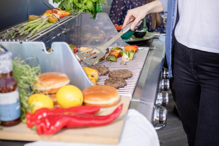 Närbild på tjej som grillar hamburgare och grillspett på Bluegaz Z1 Gasolgrill på terrass och pratar med sin väninna i bakgrunden