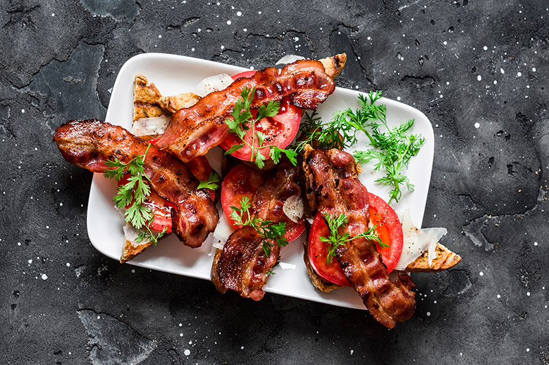 Grillad bacon med tomatskivor på vit tallrik
