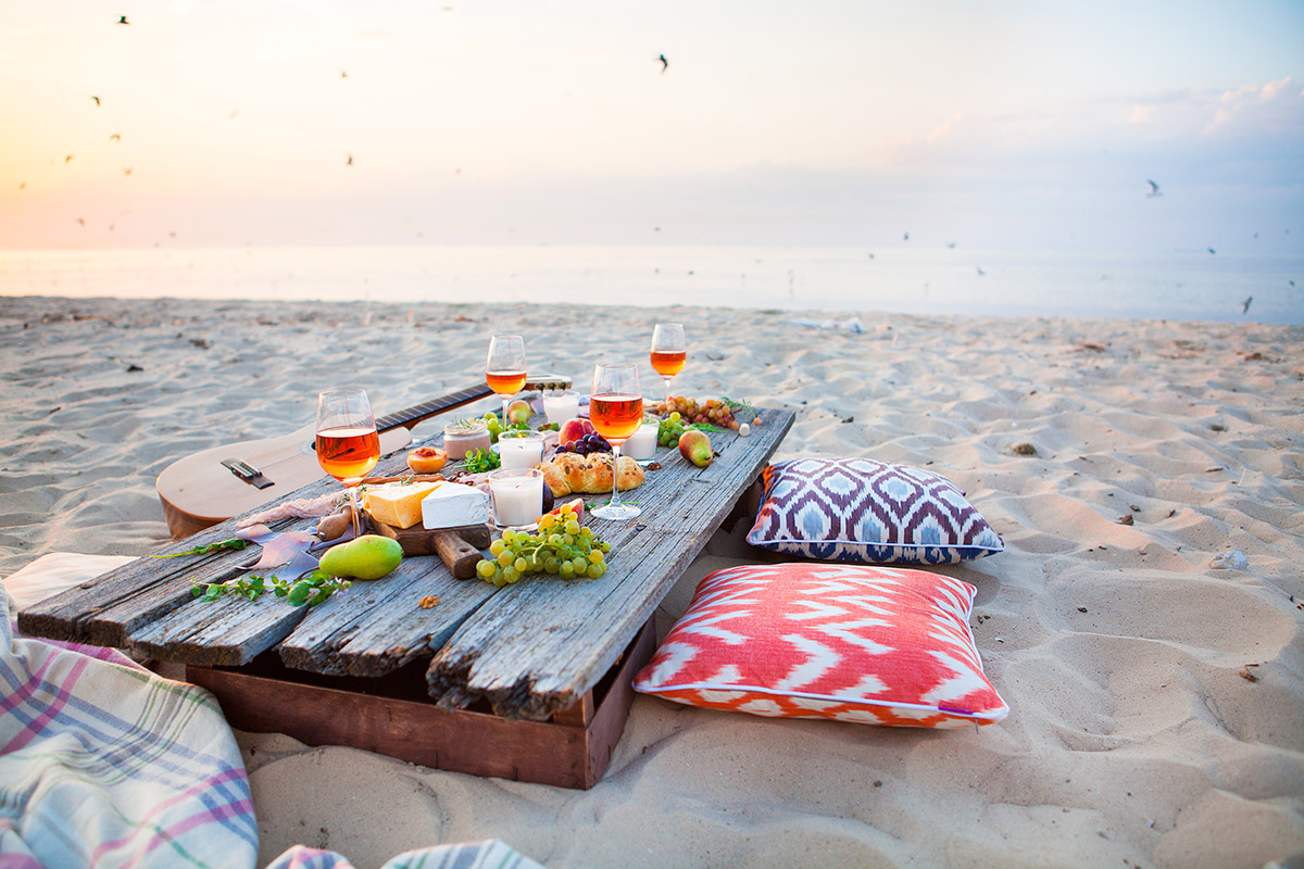 Träplanka på stranden står uppdukad med vindruvor, ost, frukt och vinglas