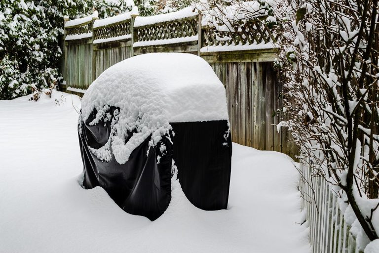 Gasolgrill med grillöverdrag täckt av snö utomhus