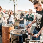 Man grillar korv på BarrelQ Grilltunna med sällskap i bakgrunden