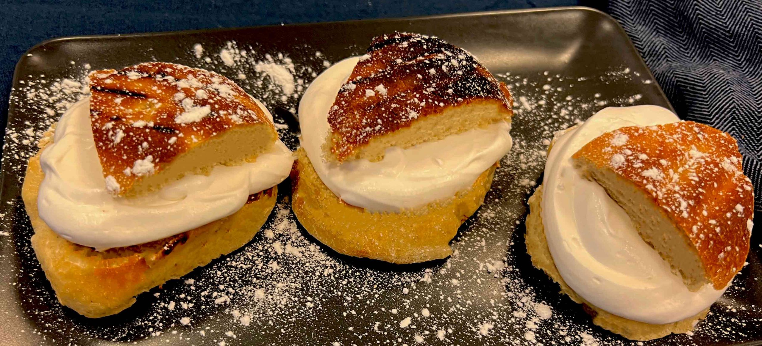 tre grillade semlor med florsocker på en grå tallrik