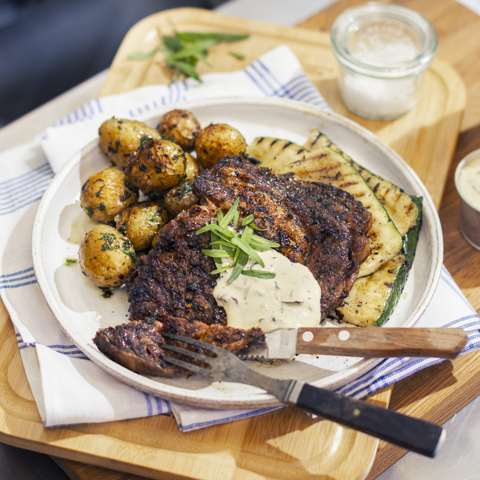 Grillad entrecôte med örtpotatis och snabblagad bearnaise på vit tallrik ovanpå skärbräda i trä