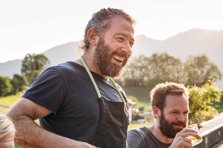 Man iklädd Höfats Grillförkläde serverar grillad mat från bricka under grillfest