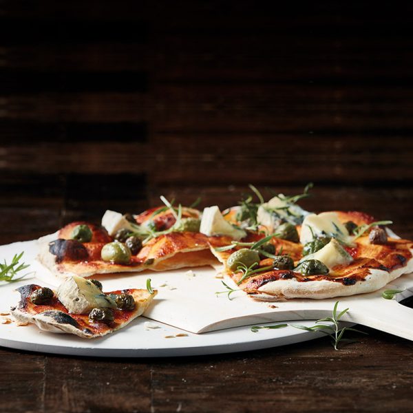 Funktion pizzaspade på vit tallrik med gorgonzolapizza med gröna och svarta oliver