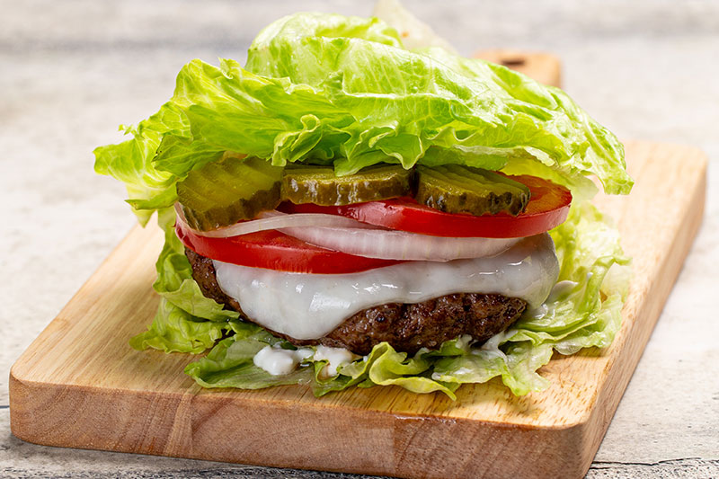 Grillad LCHF-hamburgare wrappad i salladsblad med smält vit ost, lök, tomat och bostongurka