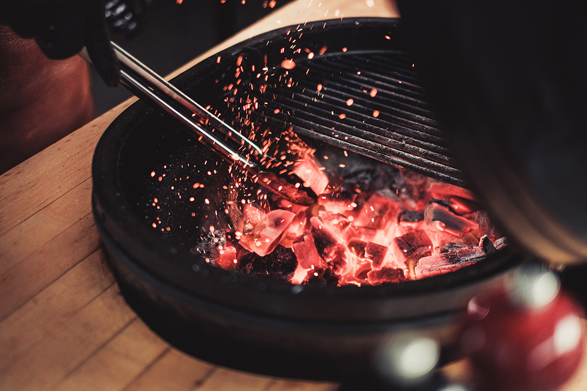 Använder grilltång för att flytta briketter i brinnande kamadogrill