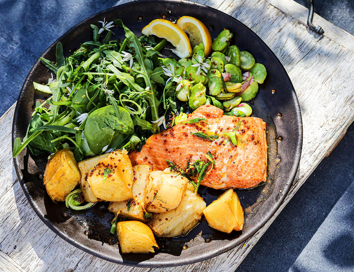 Het varmrökt laxsallad med nypotatis, bondbönor och ruccola på svart tallrik