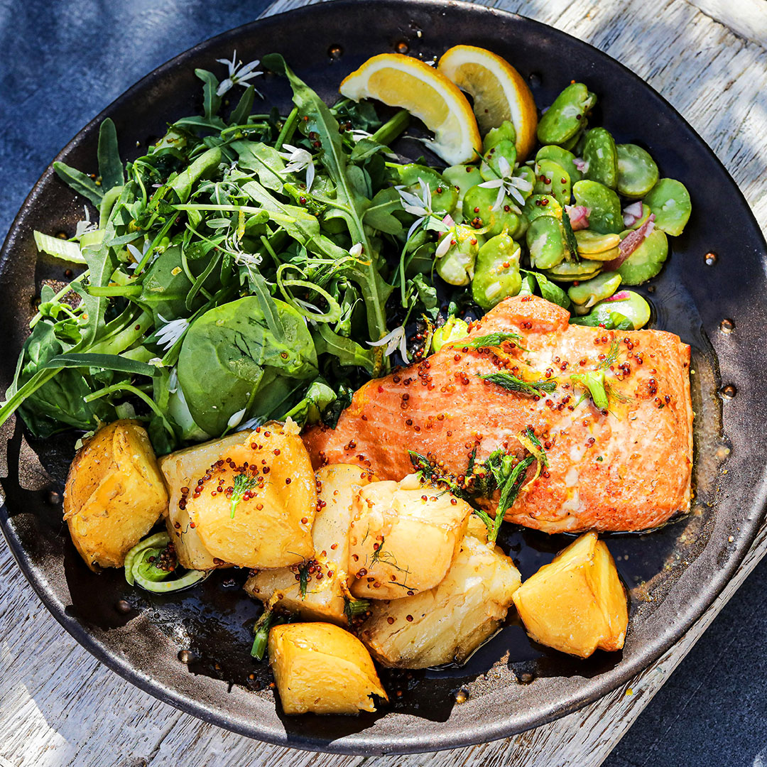 Het varmrökt laxsallad med nypotatis, bondbönor och ruccola på svart tallrik