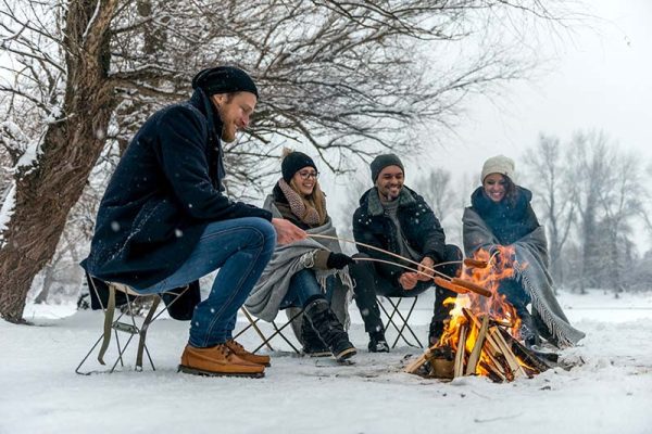 Fyra vänner grillar korv på pinne ovanför öppen eld vintertid