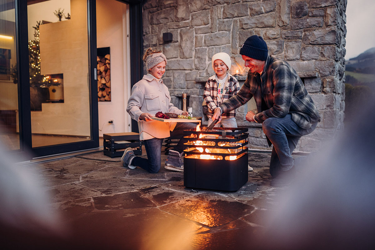 Pappa och två barn grillar med Cube Eldkorg & Kolgrill svart hösttid