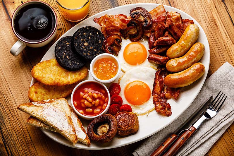 English breakfast med korv, bacon, bönor, och kaffe på träbord