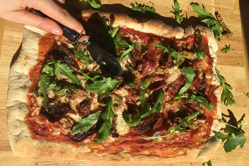 Grillad pizza på skärbärda i trä som är hälften vegan pizza och hälften pizza med lufftorkad skinka