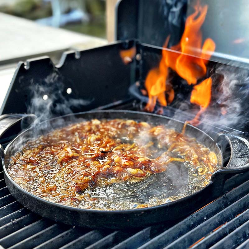 Whiskylök steks i gjutjärnspanna på grillen.