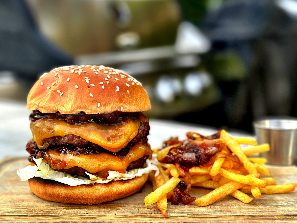 Helgrillad dubbelburgare med whiskylök och smält ost bredvid pommes på skärbricka