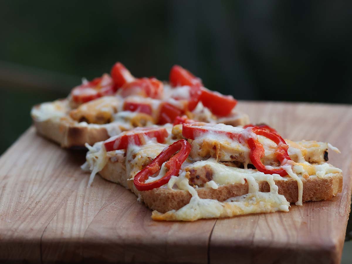 Två stycken grilled chicken sandwich med paprika, cocktailtomater och ost på skärbräda