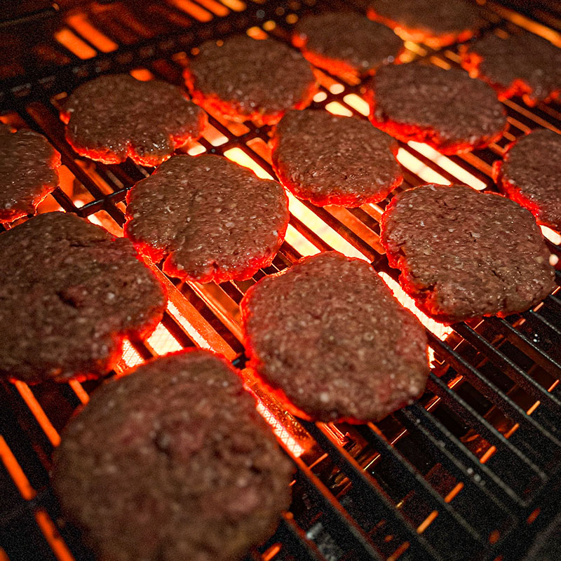 Hamburgare grillas över infraröda brännare på gasolgrill