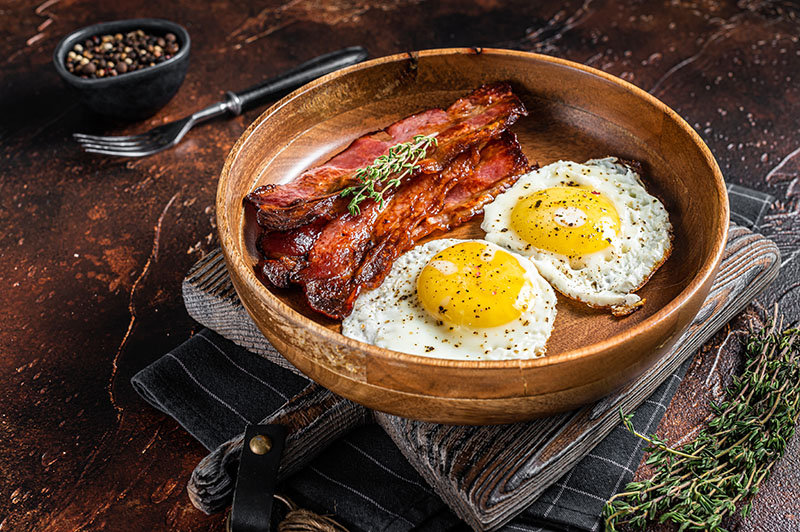 Engelsk frukost med stekt ägg och bacon i djup träskål