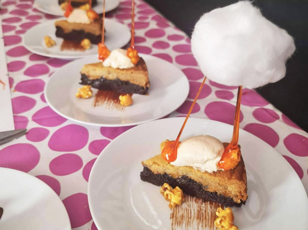 Bakad guldbrownies med färskostcrème och karamelliserade popcorn på vita tallrikar