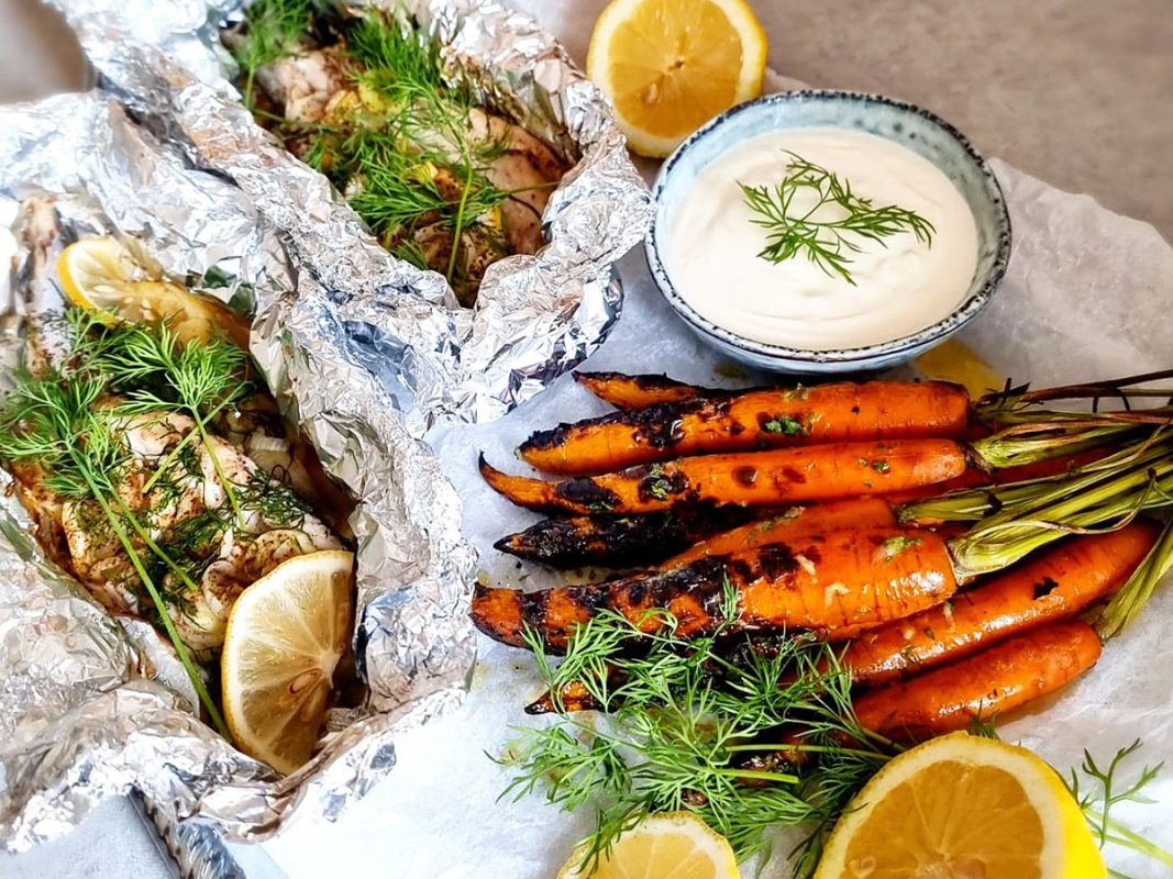 Grillad makrill i folie bredvid grillade morötter och skål med vitlökssmör