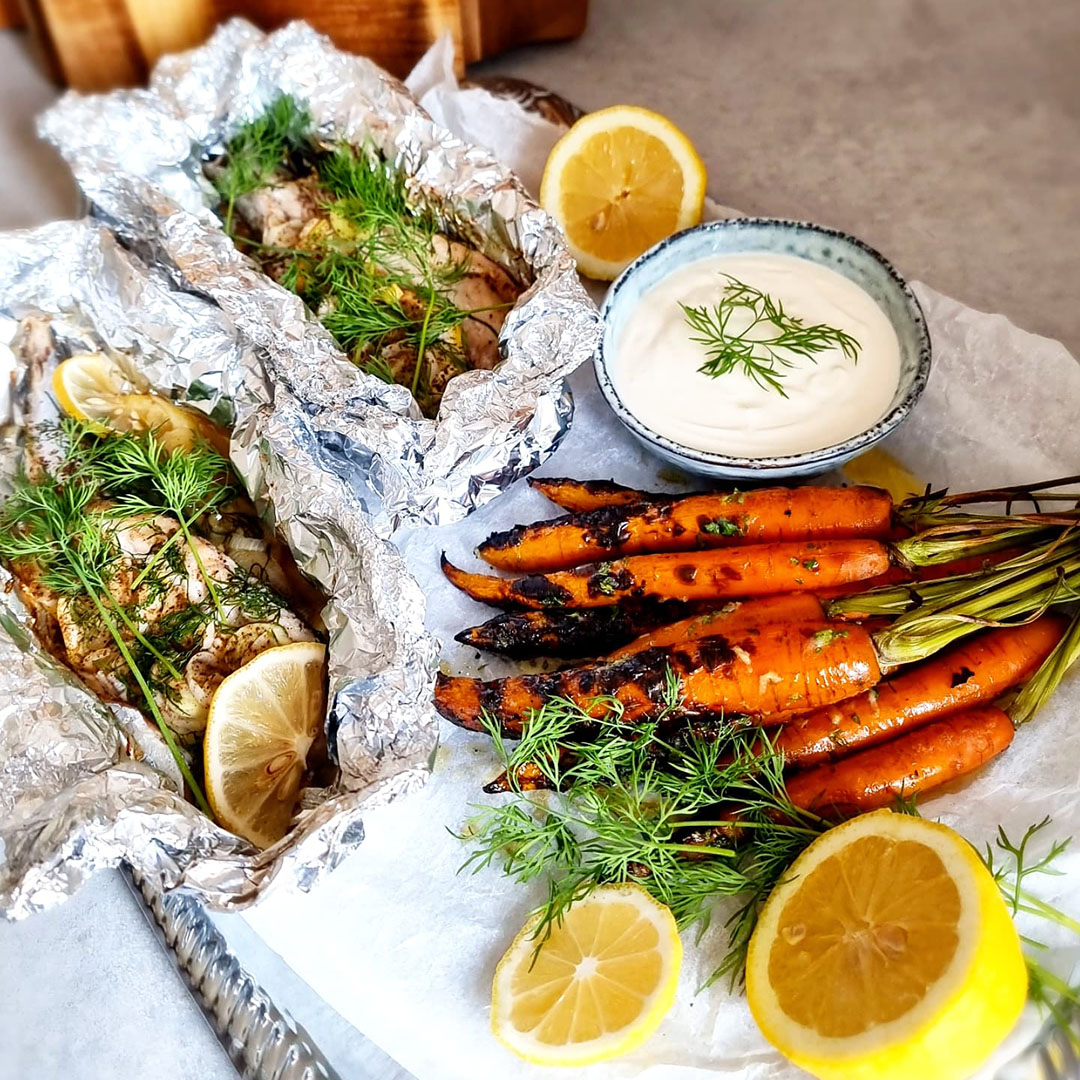 Grillad makrill i folie bredvid grillade morötter och skål med vitlökssmör