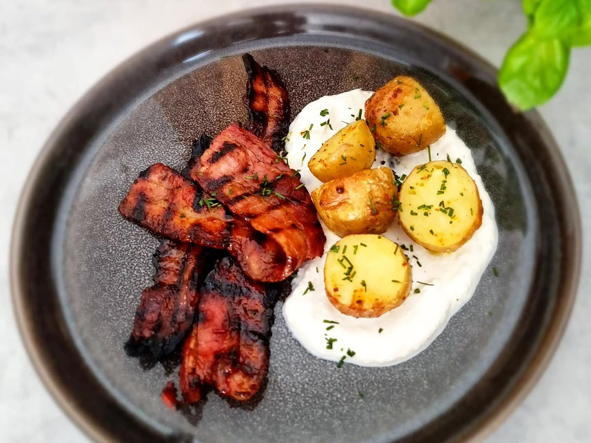 Honungs- och chilipenslat grillat fläsk med färskpotatis och parmesankräm på svart tallrik