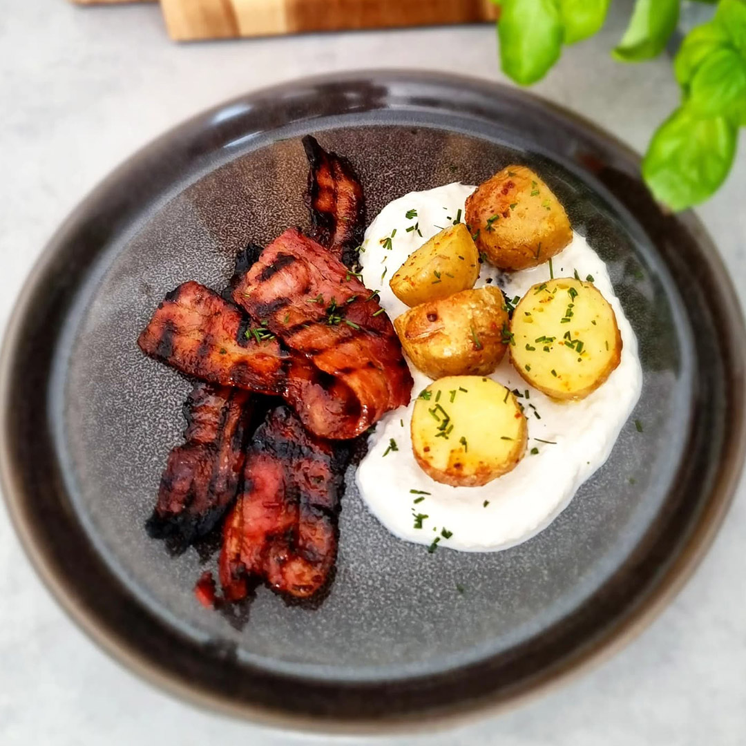 Honungs- och chilipenslat grillat fläsk med färskpotatis och parmesankräm på svart tallrik