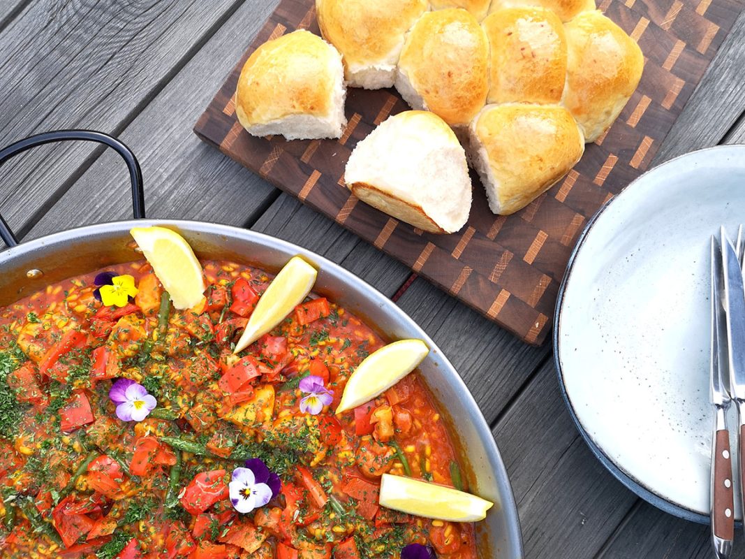 Paella med kyckling och chorizo på bord med brytbart bröd bredvid på skärbräda