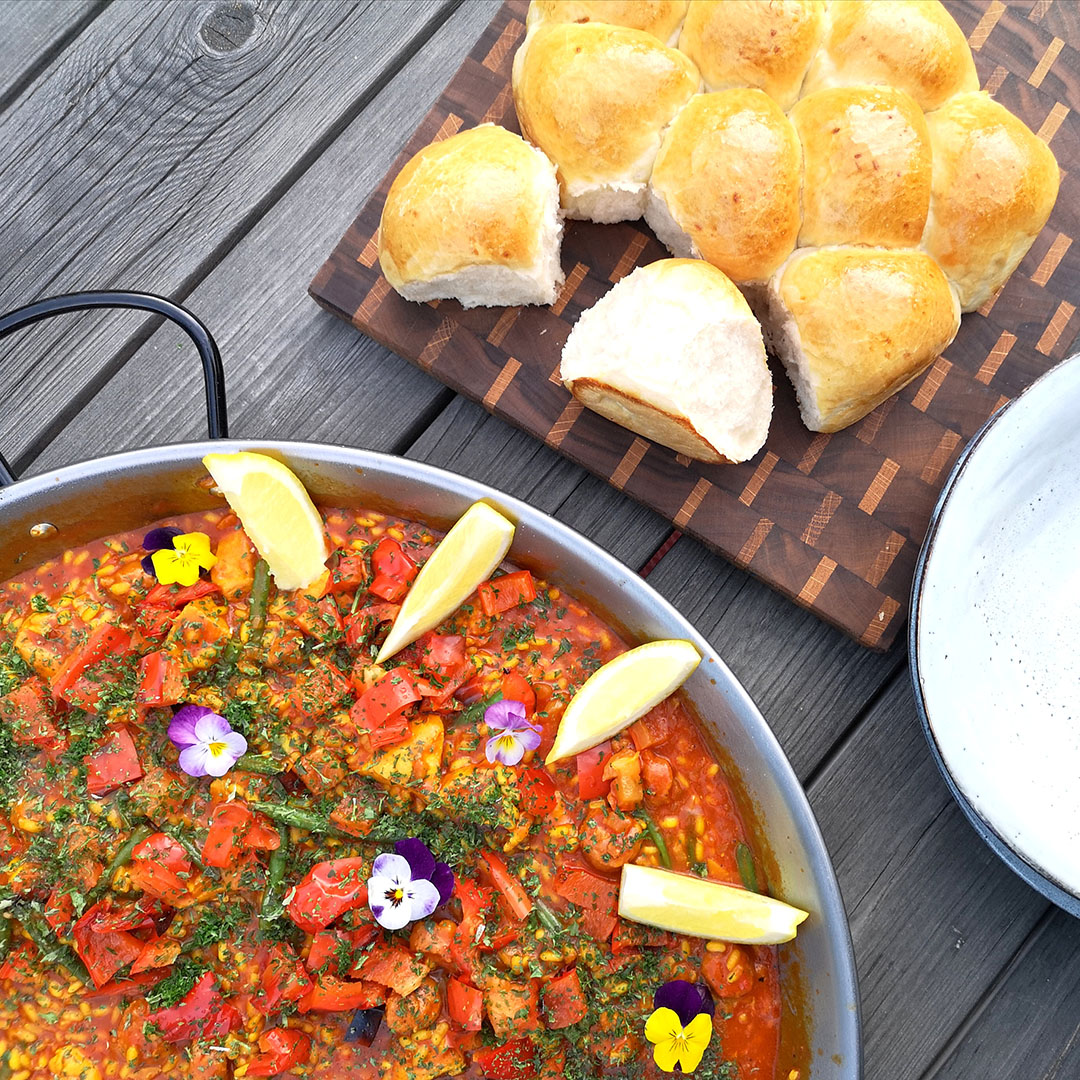 Paella med kyckling och chorizo på bord med brytbart bröd bredvid på skärbräda