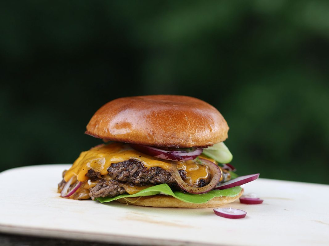 Grillad smashburger med cheddarost och picklad rödlök mot grön bakgrund