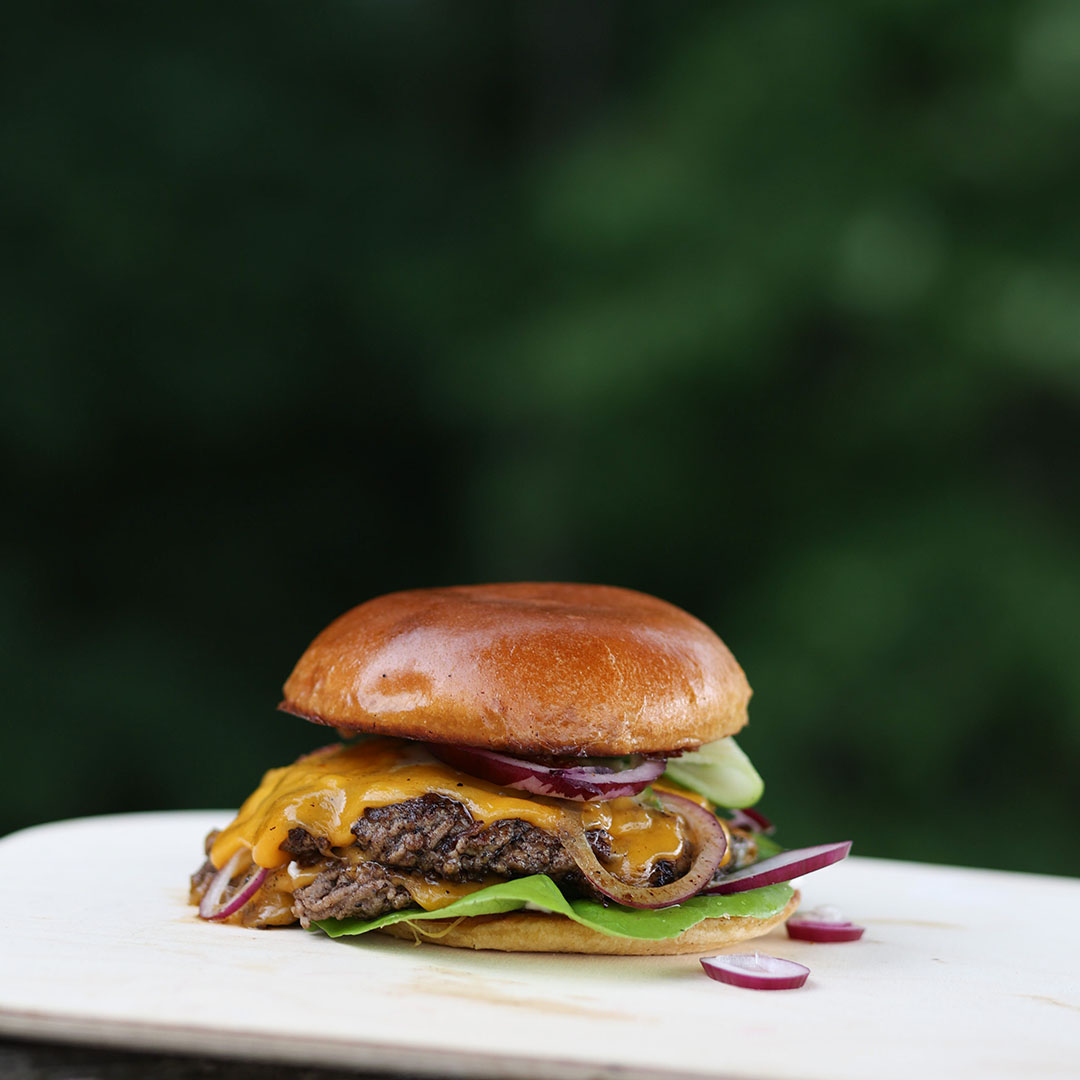 Grillad smashburger med cheddarost och picklad rödlök mot grön bakgrund