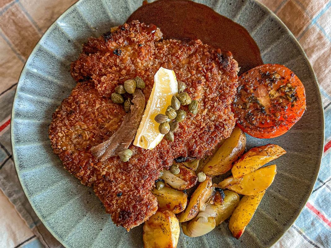 Panerad schnitzel med klyftpotatis och rödvinssås på grön tallrik