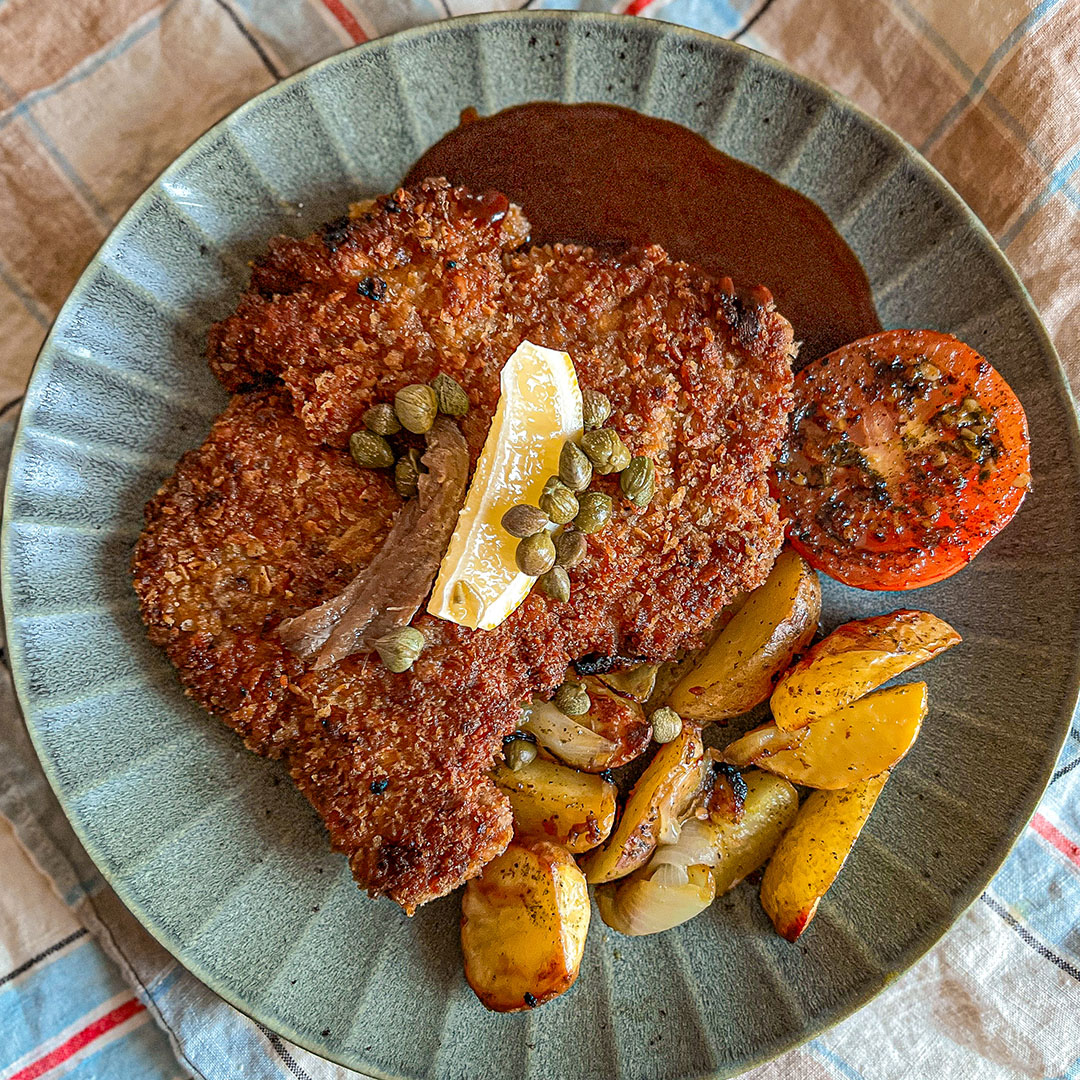 Panerad schnitzel med klyftpotatis och rödvinssås på grön tallrik