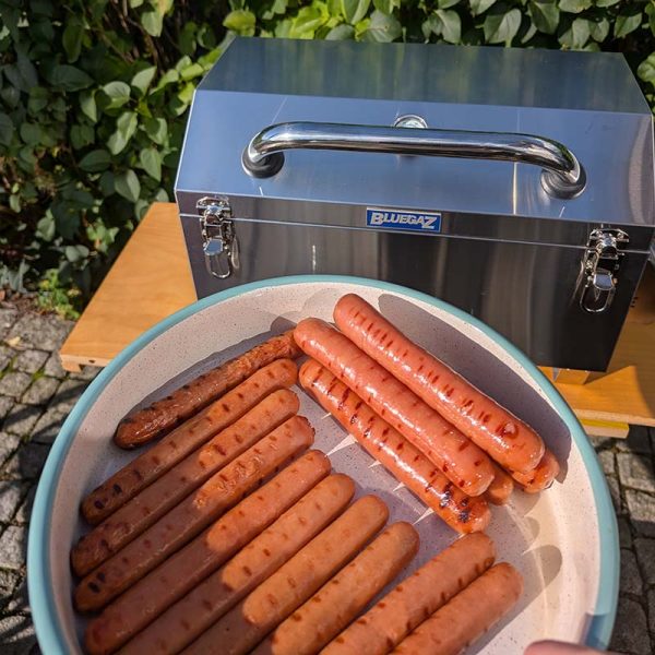 Håller tallrik med korv framför Bluegaz T10 Bärbar gasolgrill