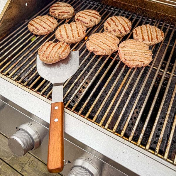 Bluegaz Elite Burger Flipper ligger på grillgaller bredvid burgare