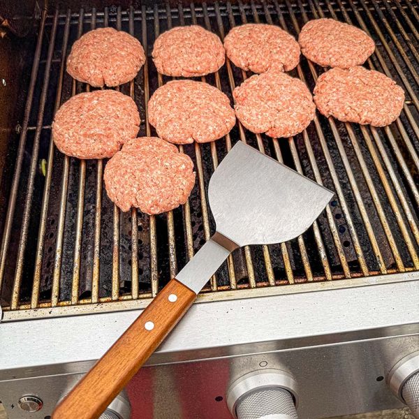 Bluegaz Elite Burger Flipper ligger på grillgaller framför burgare