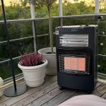 Bluegaz Tabernas Gasolkamin med fläkt står på trädäck bredvid vit kruka med rosa blommor