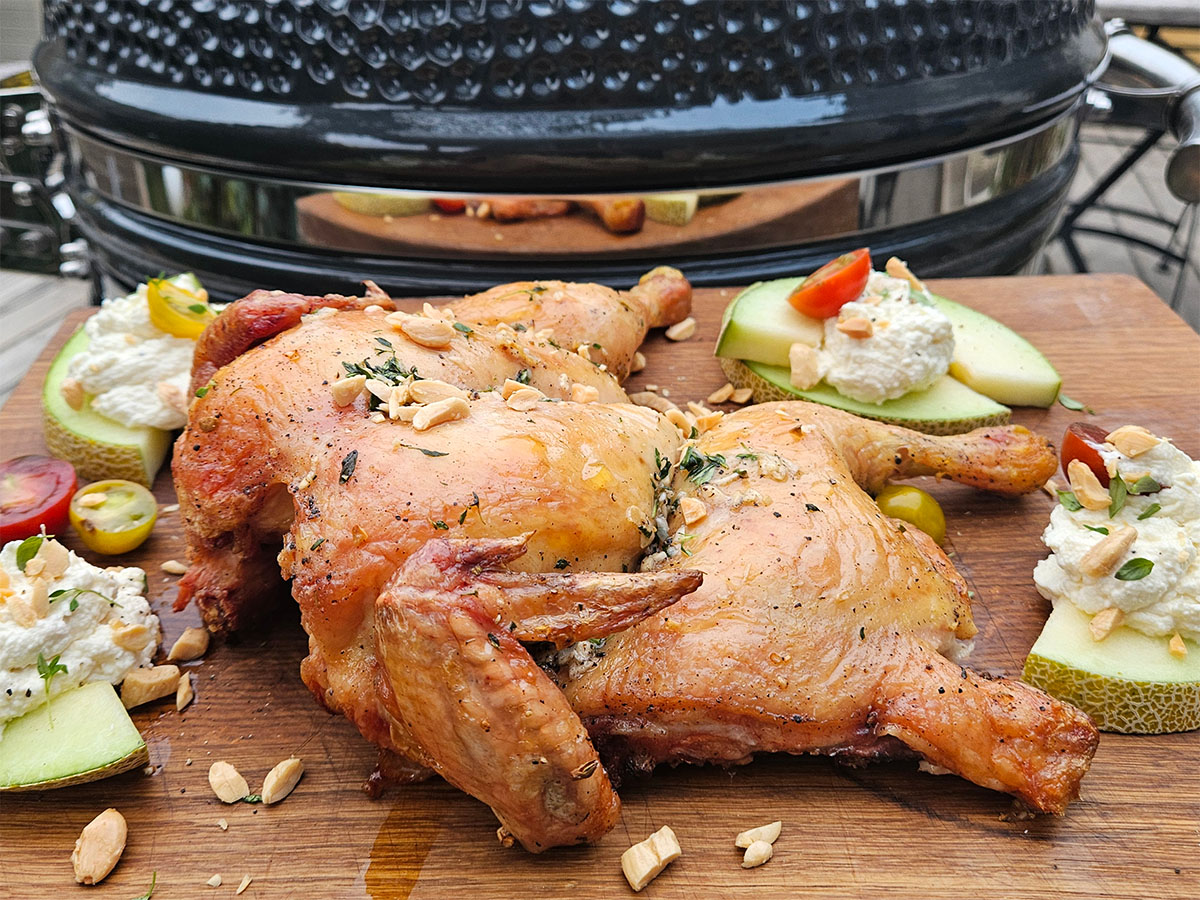 Grillad hel kyckling på skärbräda framför kamadogrill