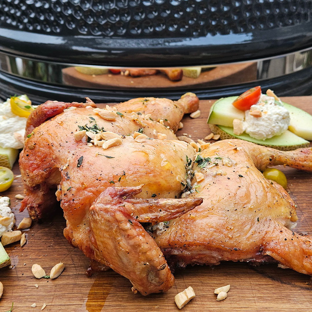 Grillad hel kyckling på skärbräda framför kamadogrill