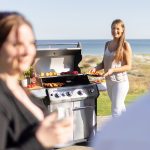Ung kvinna står bredvid Bluegaz X1 Gasolgrill med havet i bakgrunden