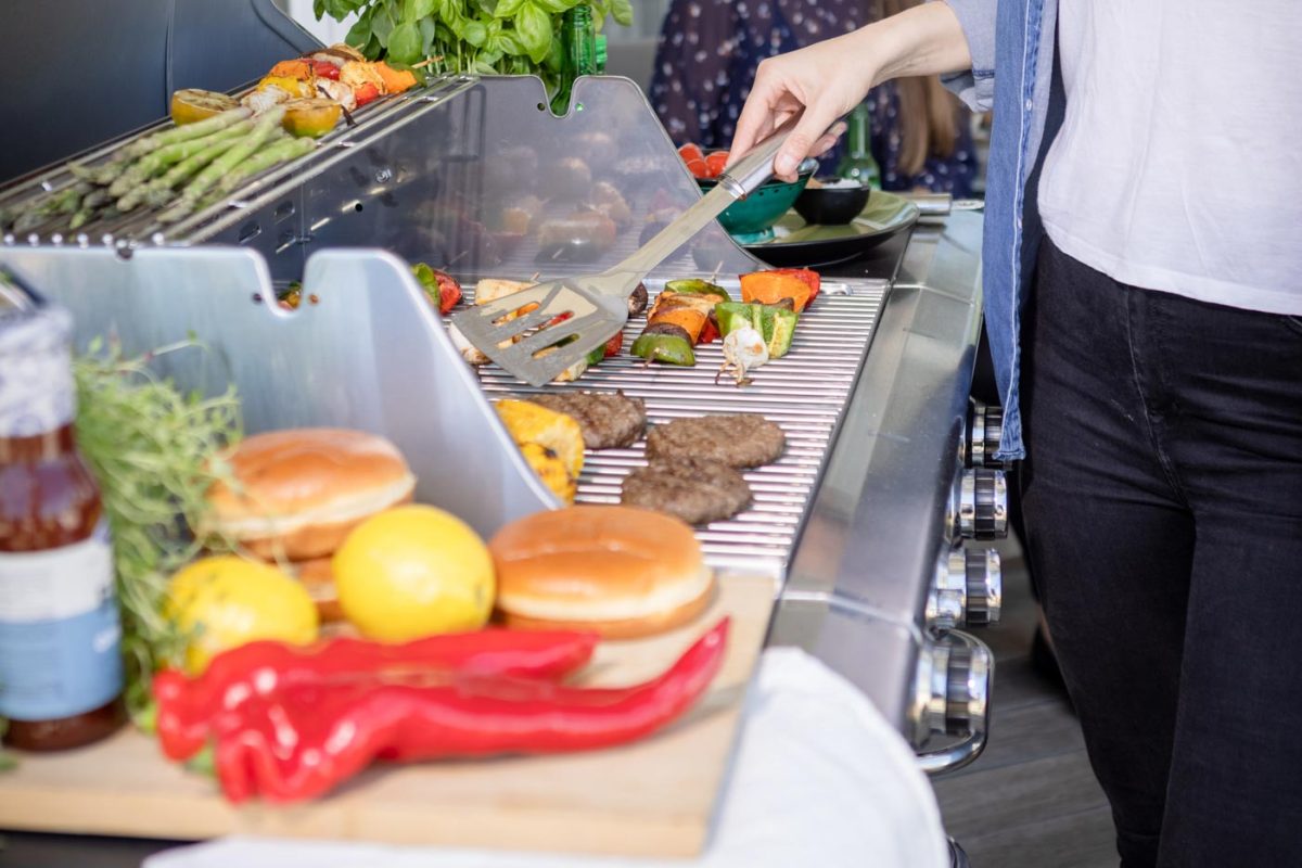 Närbild på tjej som grillar hamburgare och grillspett på Bluegaz Z1 Gasolgrill på terrass och pratar med sin väninna i bakgrunden