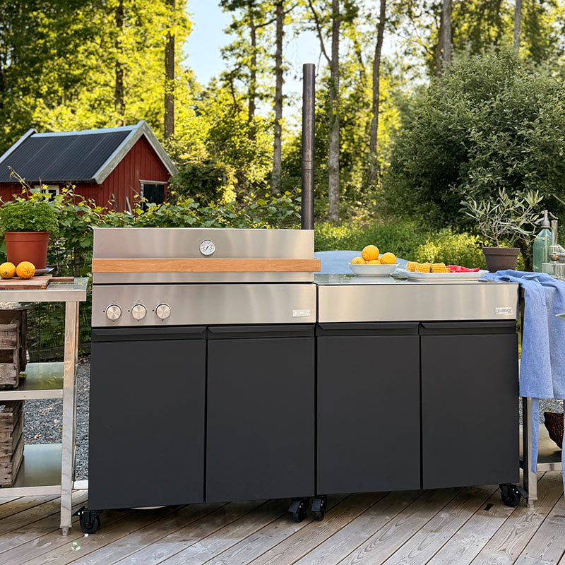 Bluegaz Z Gasolgrill med Z Sidomodul på trädäck med grönska och röd stuga i bakgrunden