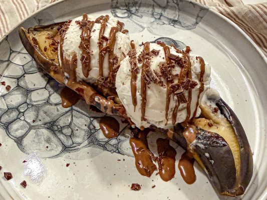 Grillad banan med smält choklad och glass med krossad choklad på tallrik