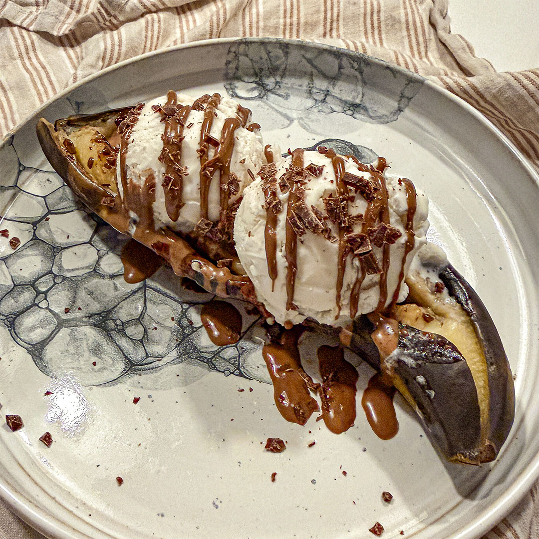 Grillad banan med smält choklad och glass med krossad choklad på tallrik