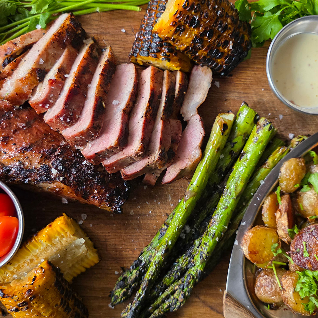 Grillad pluma med smörstekt potatis, majskolv, sparris och citronaioli på träskärbräda